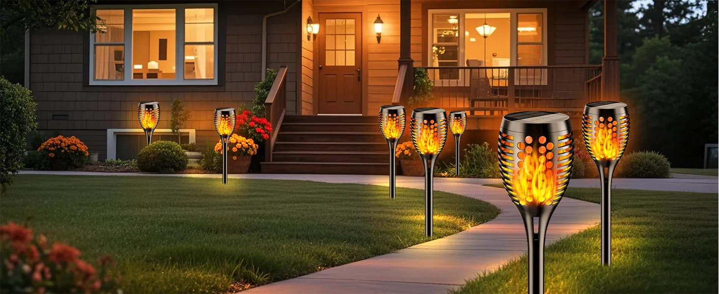 Decorative solar torch lights with flickering flame effect illuminating a garden pathway at dusk.
